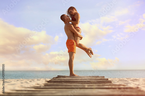 Young woman in bikini spending time with her boyfriend on beach. Lovely couple