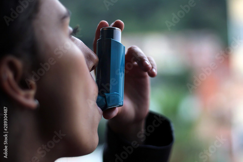 Health and medicine - Young girl using blue asthma inhaler to prevent an asthma attack.
