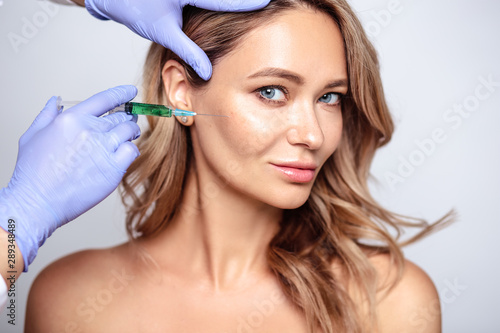 Close up portrait of blonde woman with cosmetologist hands near her face. Procedure in salon, spa and care