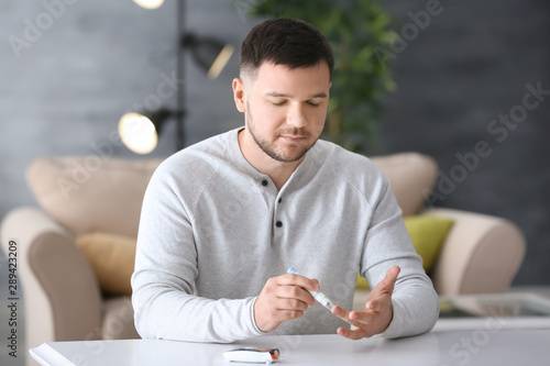 Diabetic man taking blood sample with lancet pen at home