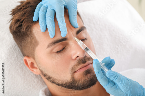 Handsome man receiving filler injection in beauty salon