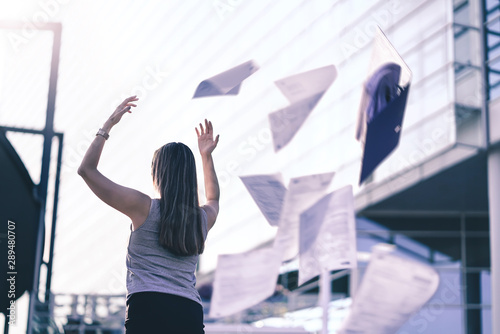 Business woman throwing work papers in the air. Stress from workload. Person going home or leaving for vacation. Employee got fired. Job or project done. Difficult workday over. Outside of office.