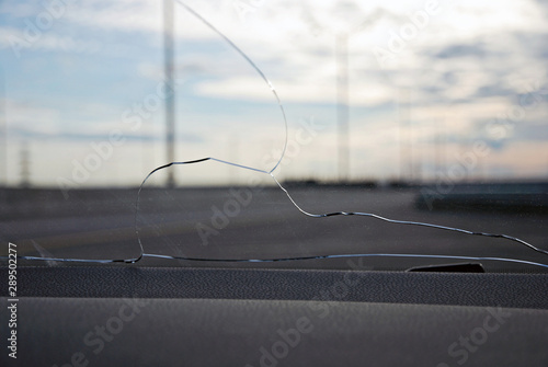 Cracks on car windshield glass hit by stone ejected from under the wheels of another car. View from inside against empty freeway