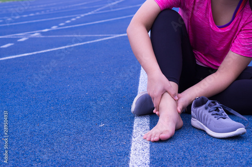 Ankle sprained. Young woman suffering from an ankle injury while jogging and running on running track. Healthcare and sport concept.
