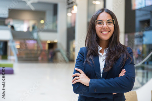 Young businesswoman smiling at camera. Portrait of cheerful Hispanic businesswoman in formal wear standing with crossed arms and looking at camera. Business concept