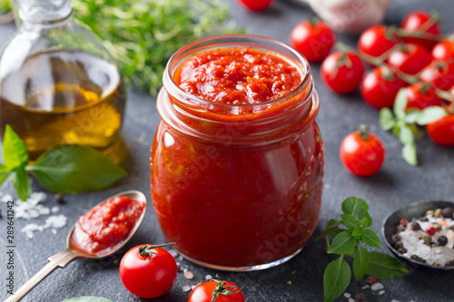 Tomato sauce in a glass jar with fresh herbs, tomatoes and olive oil.