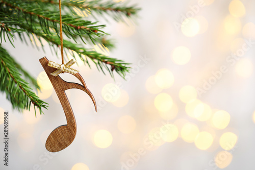 Fir tree branch with wooden note against blurred lights, space for text. Christmas music