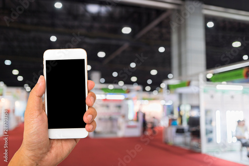 Hand hold blank smartphone on blue exhibition hall background