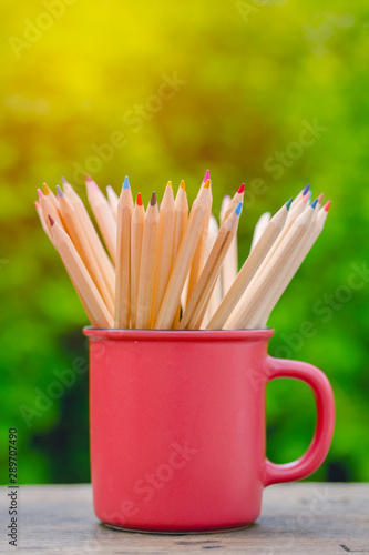 Group of color pencil in glass on table with blur garden background