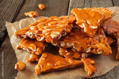 Pile of traditional peanut brittle candy pieces. Close up on an old dark wood background.