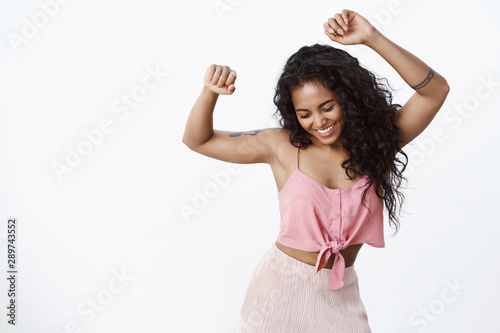 Fun, party, wellbeing concept. African-american curly-haired girl in trendy pink top, skirt dancing with hands spread air, smiling broadly close eyes as enjoying music with carefree expression