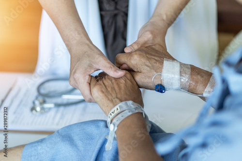 Elderly senior aged patient on bed with geriatric doctor holding hands for trust and nursing health care, medical treatment, caregiver and in-patient ward healthcare in hospital