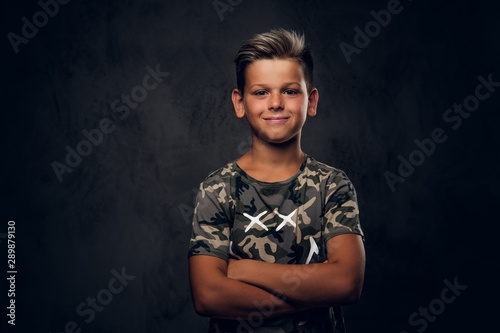 Little charming boy with nice hairstyle is posing over dark background at photo studio.