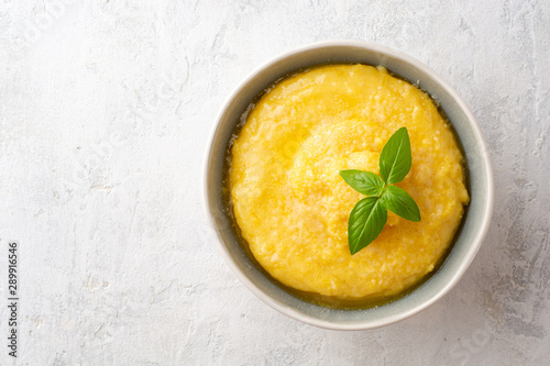 Polenta with butter and parmesan cheese in bowl on concrete background. Top view. Copy space.