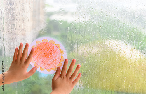 kid holding picture of a smiling sun in a raining day concept of faith and optimism