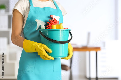 Female janitor with set of cleaning supplies in office