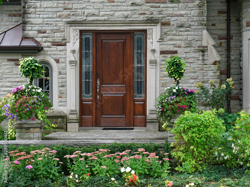 stone faced house with flower garden and elegant wooden front door with sidelights