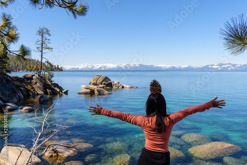 A sport woman carrying pine cone with open arms enjoys the view of Lake Tahoe with clear blue wate, California
