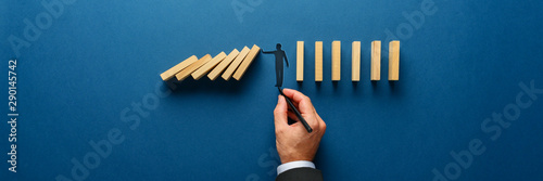 Silhouette of a man making a stop gesture to prevent wooden dominos from collapsing