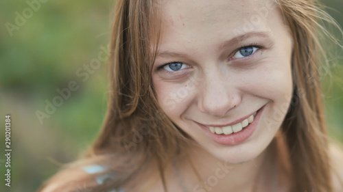 Portrait of a young smiling sixteen-year-old girl with a daisy flower in her hands. Brown-haired girl with long hair.. Face close-up.