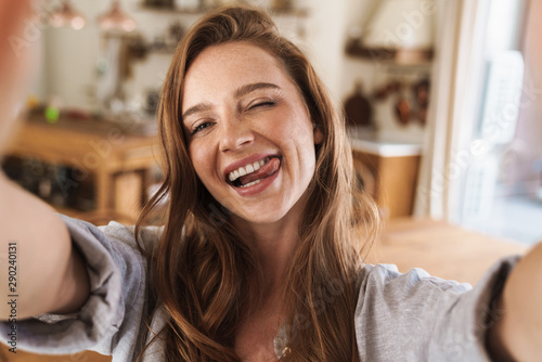 Beautiful happy ginger woman indoors at home take selfie by camera.