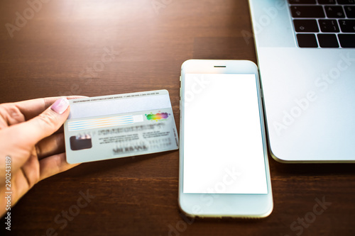 Closely woman banker holding credit debit card near mobile phone with empty mock up copy space screen background for promotional content. Online payment money via cellphone with blank display