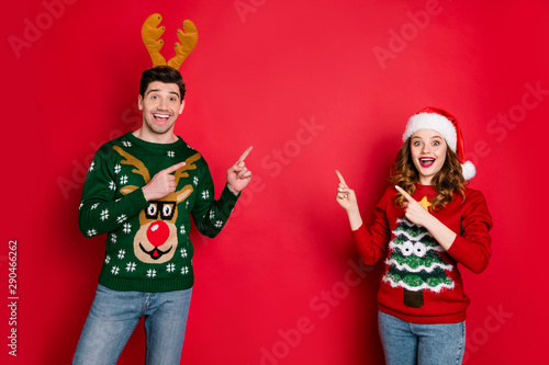 Photo of crazy lady and guy directing fingers empty space on x-mas sale wear funky ugly ornament pullovers isolated red color background