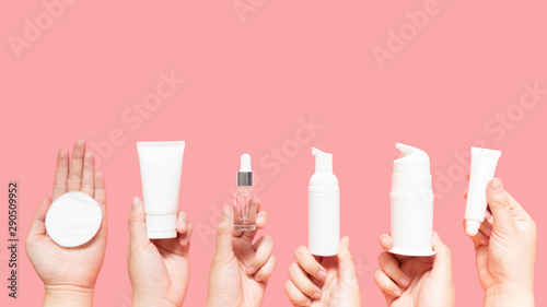 Skincare routine step for healthy skin - Woman hands holding facial cotton pad, foam, essential oil, serum, lotion and eye cream packaging on pink background. Beauty and cosmetic concept. Copy space.