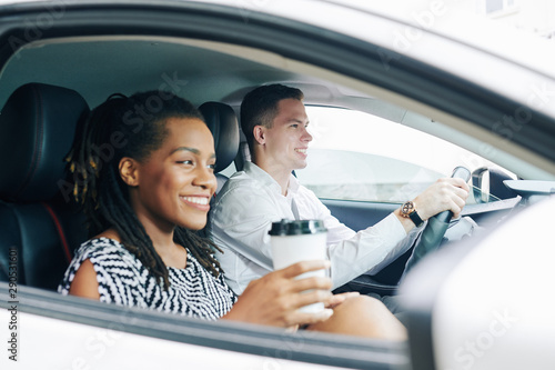 Happy African girl drinking coffee and smiling while sitting in the car with young man