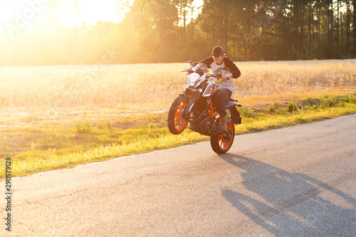 Teenage boy on a dirtbike motorcycle doing a wheelie at sunset