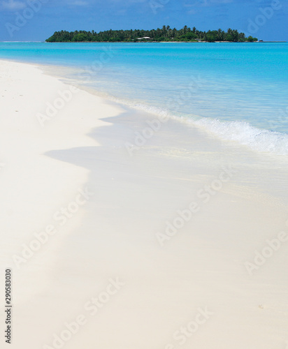 Beautiful white sand Maldivian beach and absolutely clear blue waters of Indian Ocean with a tropical paradise island on the background