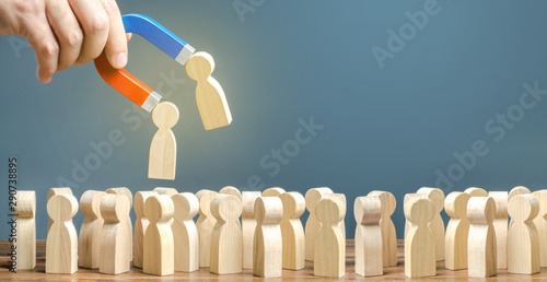 Businessman with a magnet pulls wooden figures of people out of big crowd. Recruiting workers. Formation of a new team. Search for required people and workers with the necessary talents and skills