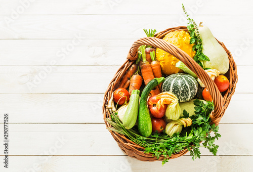 Colorful organic vegetables in wicker basket on white wood