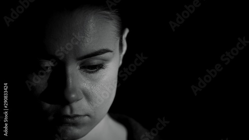 Ashamed woman looking down against dark background, humiliation victim, kidnap