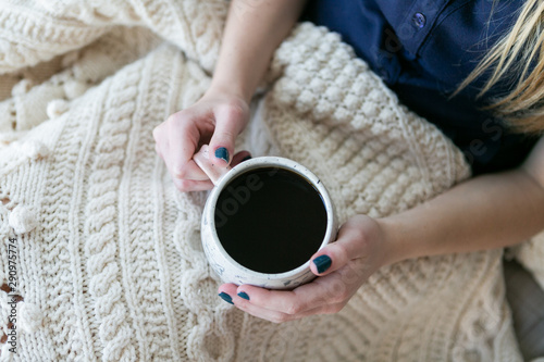 Girl holding cup of coffee in bed with white knitted blanket, cozy morning