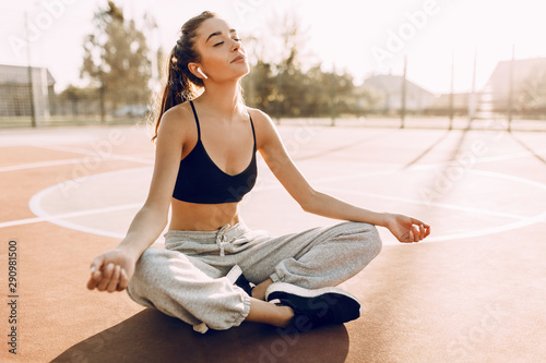 Young woman in sportswear sitting outdoors relaxing meditation taking sun rays
