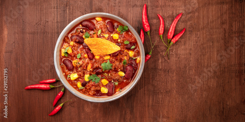 Chili con carne with chilli peppers and a nacho chip, overhead panoramic shot on a dark rustic wooden background with a place for text