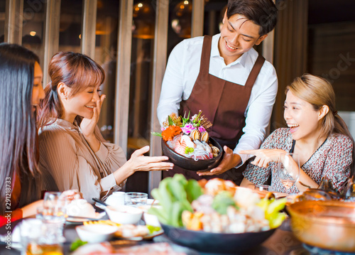 waiter bring seafood and serving group of friends in restaurant.