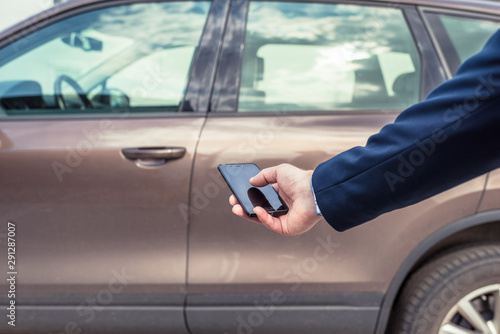 Customer hand holding mobile phone for opening car door. Car sharing service or rental concept.