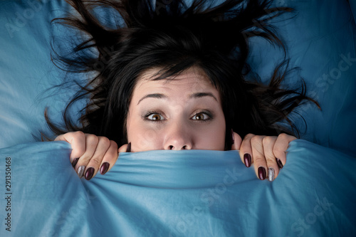 girl hides her face under the covers in bed. a nightmare after watching a horror movie. fear of nightmares