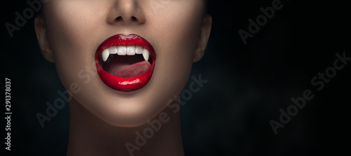 Sexy Vampire Woman's red bloody lips close-up. Vampire girl licking fangs with tongue. Fashion Glamour Halloween art design. Close up of female vampire mouth, teeth. Isolated on black background