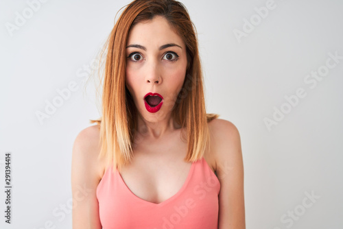 Beautiful redhead woman wearing casual pink t-shirt standing over isolated white background scared in shock with a surprise face, afraid and excited with fear expression
