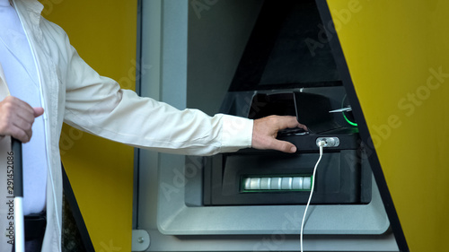 Visually impaired man inserting password on atm machine, withdrawing money