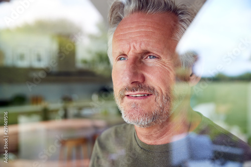 Senior Man Standing And Looking Out Of Kitchen Door Viewed Through Window