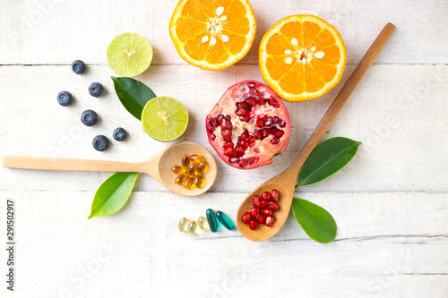 Multivitamin supplements on wooden spoon with healthy fruit blueberry, lime, orange, pomegranete on white wooden background.