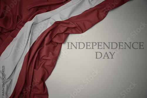 waving colorful national flag of latvia on a gray background with text independence day.