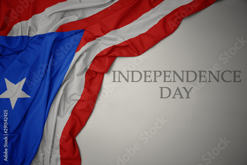 waving colorful national flag of puerto rico on a gray background with text independence day.