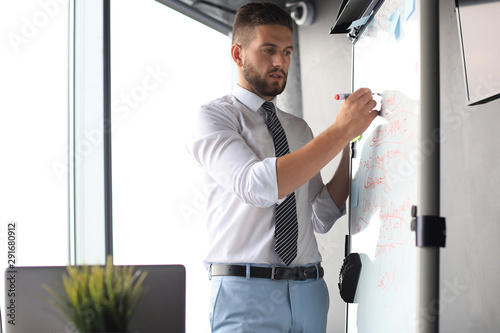 Smart concentrated businessman writing something on the flipchart using marker