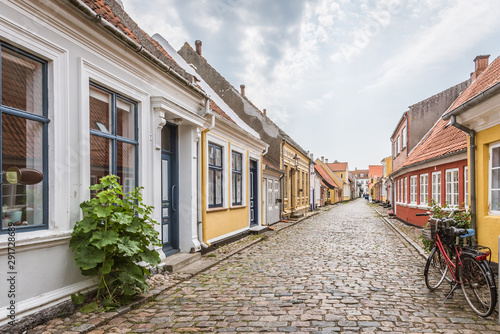 A red bike standing alone in an cobblestone street with romantic houses on the island Aero