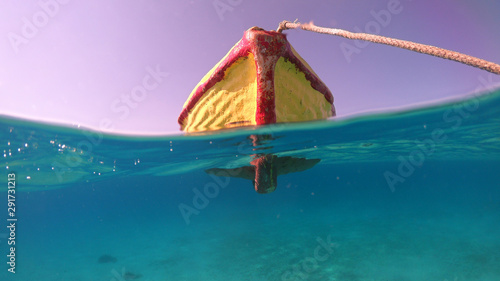 Above and below underwater photo of traditional fishing boat docked in turquoise clear sea, Mykonos island, Cyclades, Greece
